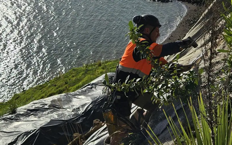 Technician securing a steep coastal slip face with temporary weather protection